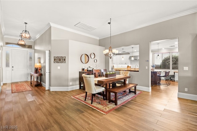 dining space with ornamental molding, an inviting chandelier, sink, and hardwood / wood-style flooring