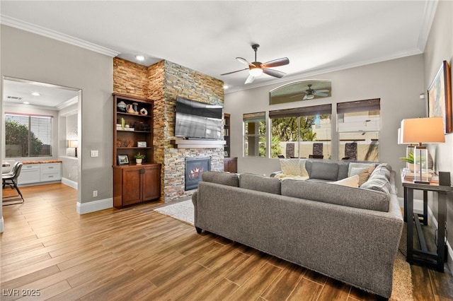 living room featuring hardwood / wood-style floors, ceiling fan, ornamental molding, and a stone fireplace