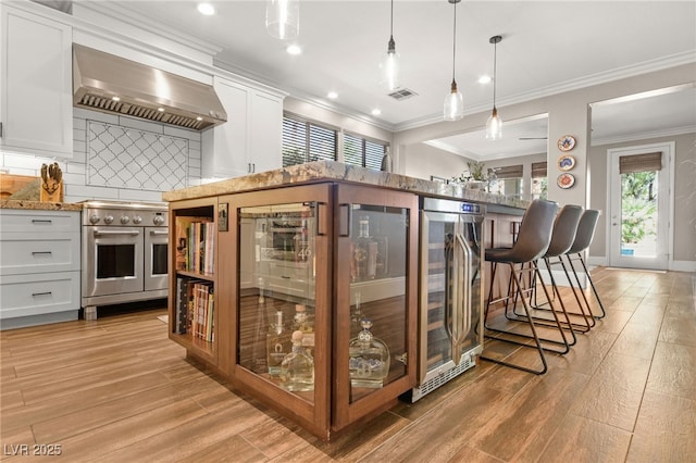 kitchen with range with two ovens, wine cooler, backsplash, white cabinets, and ventilation hood