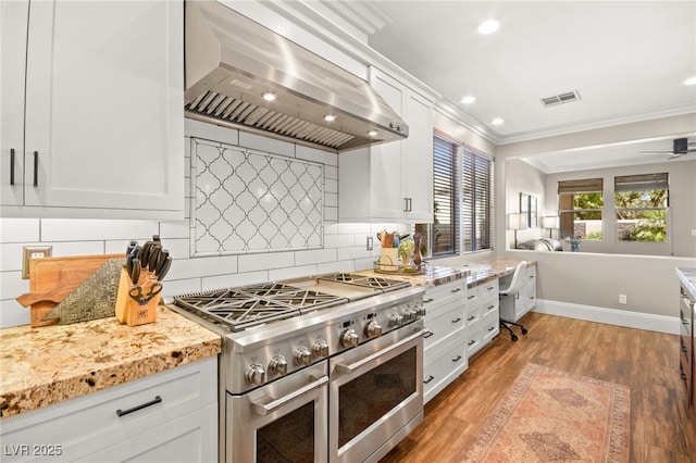 kitchen featuring range hood, double oven range, decorative backsplash, light wood-type flooring, and white cabinets