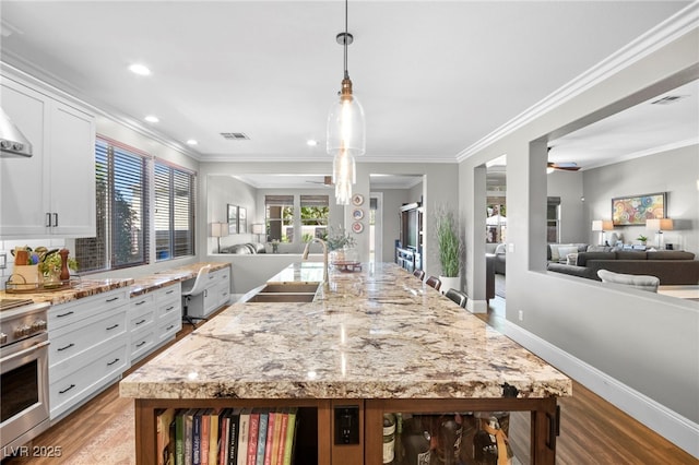 kitchen with oven, white cabinetry, pendant lighting, and light stone counters