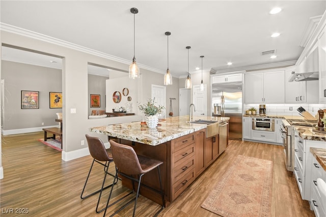 kitchen with a kitchen island with sink, ornamental molding, white cabinets, sink, and premium appliances