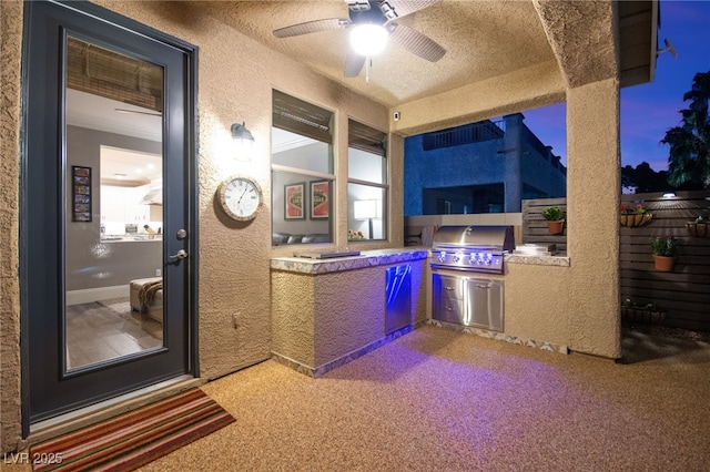 patio terrace at dusk with ceiling fan, a grill, and an outdoor kitchen