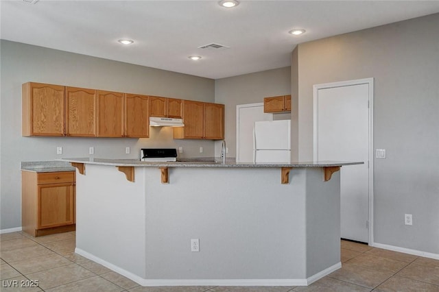 kitchen with white fridge, an island with sink, light tile patterned flooring, stove, and sink