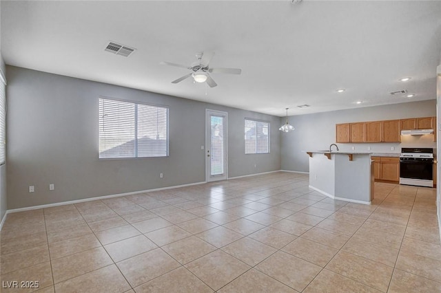 unfurnished living room featuring ceiling fan with notable chandelier, light tile patterned flooring, and plenty of natural light