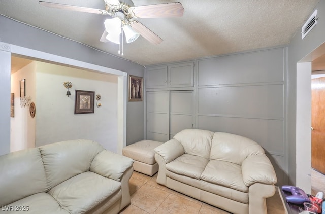 living room with a textured ceiling, ceiling fan, and light tile patterned floors