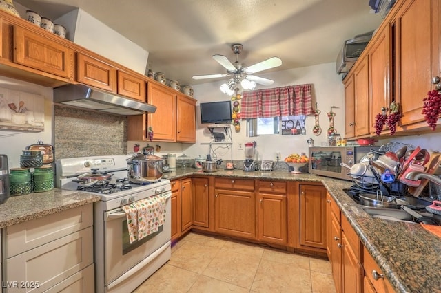 kitchen featuring dark stone counters, sink, white range with gas cooktop, and light tile patterned floors