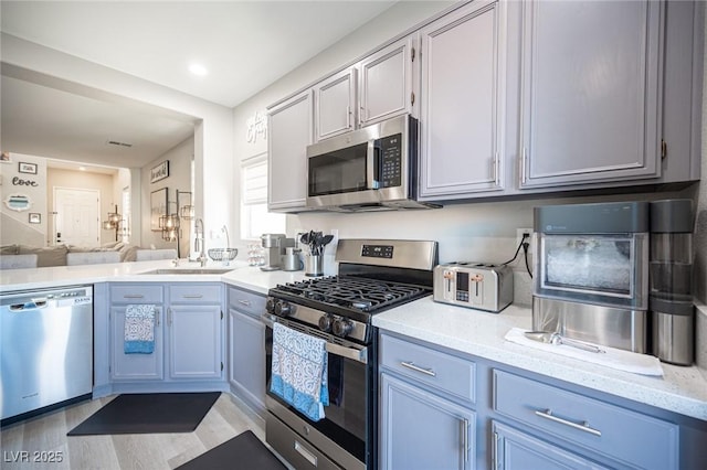 kitchen featuring stainless steel appliances, sink, light wood-type flooring, and light stone counters