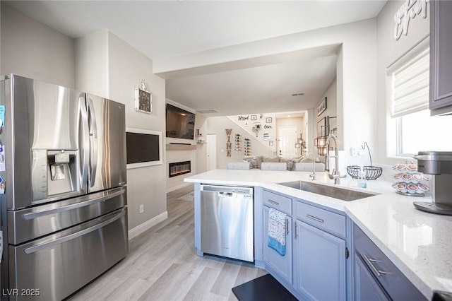 kitchen featuring kitchen peninsula, light hardwood / wood-style floors, blue cabinetry, appliances with stainless steel finishes, and sink