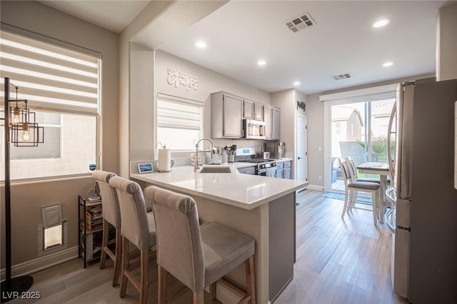 kitchen featuring kitchen peninsula, light hardwood / wood-style flooring, appliances with stainless steel finishes, a kitchen breakfast bar, and sink