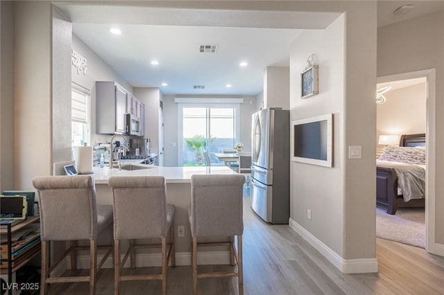 kitchen with stainless steel appliances, light wood-type flooring, kitchen peninsula, a kitchen bar, and sink