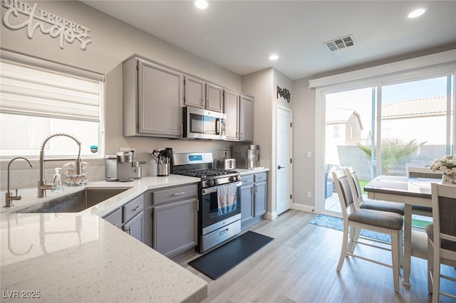 kitchen featuring stainless steel appliances, light hardwood / wood-style floors, gray cabinetry, and sink