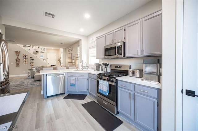 kitchen with stainless steel appliances, sink, light hardwood / wood-style floors, and kitchen peninsula