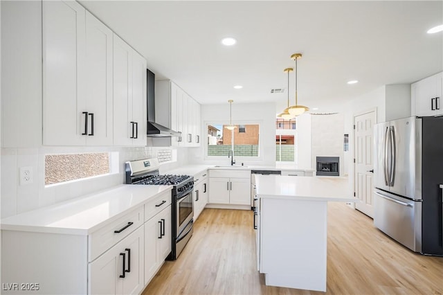 kitchen featuring white cabinets, wall chimney exhaust hood, tasteful backsplash, hanging light fixtures, and appliances with stainless steel finishes