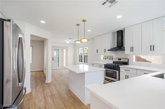 kitchen featuring stainless steel appliances, hanging light fixtures, a kitchen island, white cabinets, and wall chimney range hood