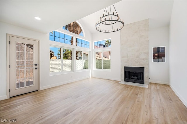 unfurnished living room with light hardwood / wood-style flooring, a chandelier, a towering ceiling, and a fireplace