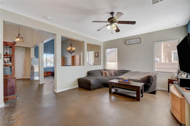 living room featuring ceiling fan with notable chandelier, a wealth of natural light, and concrete flooring