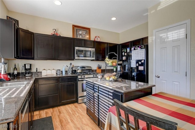 kitchen featuring a center island, dark stone countertops, light hardwood / wood-style flooring, dark brown cabinets, and appliances with stainless steel finishes