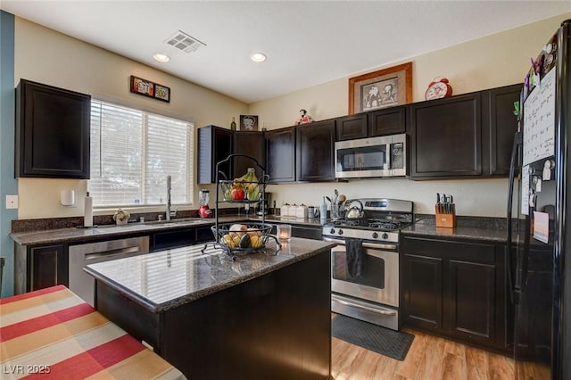 kitchen featuring appliances with stainless steel finishes, dark stone counters, a kitchen island, sink, and light hardwood / wood-style flooring