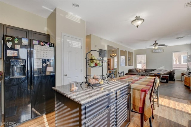 kitchen with black fridge, light wood-type flooring, a kitchen island, and ceiling fan with notable chandelier