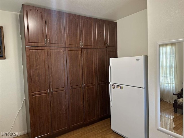 kitchen with white refrigerator, light wood-type flooring, and dark brown cabinetry