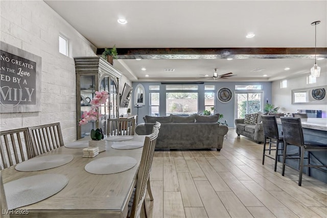 dining area featuring ceiling fan, a large fireplace, and beam ceiling