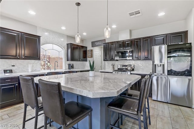 kitchen featuring tasteful backsplash, dark brown cabinets, a kitchen island, pendant lighting, and appliances with stainless steel finishes