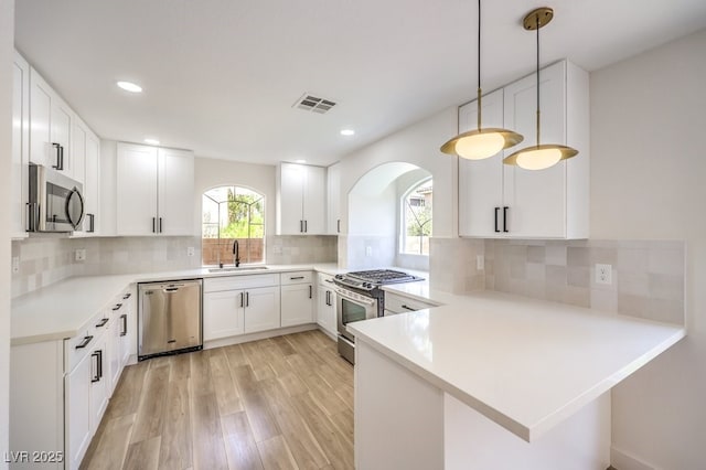 kitchen with stainless steel appliances, sink, white cabinetry, kitchen peninsula, and hanging light fixtures