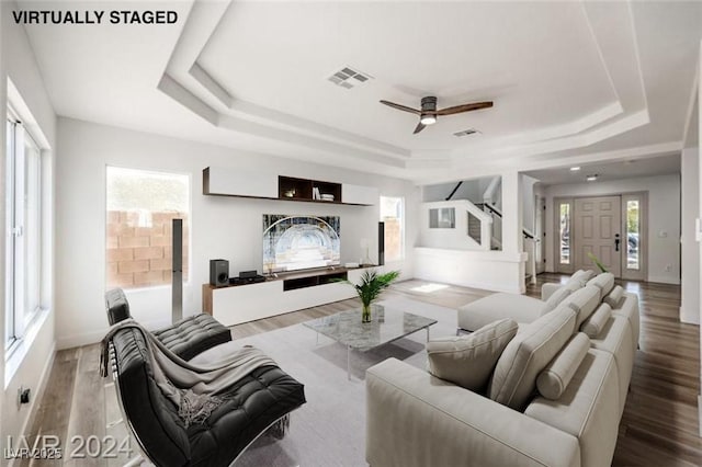 living room with wood-type flooring, ceiling fan, and a tray ceiling