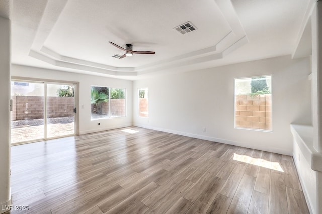 unfurnished room with ceiling fan, light hardwood / wood-style flooring, a wealth of natural light, and a raised ceiling