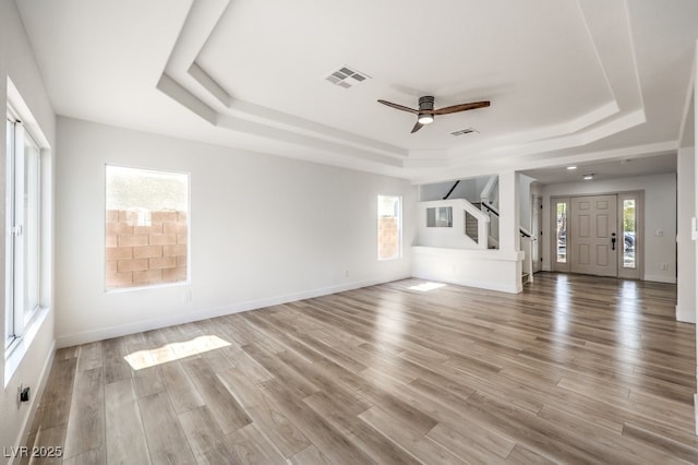 unfurnished living room with light wood-type flooring, ceiling fan, and a tray ceiling