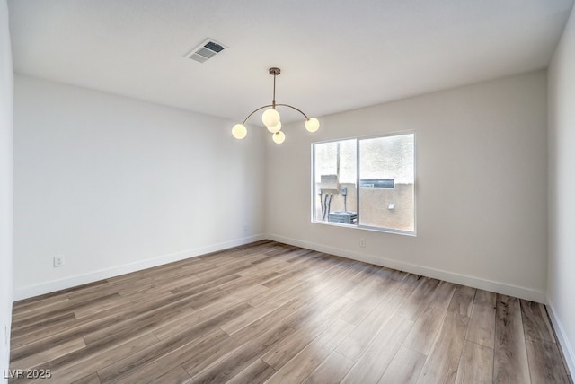 spare room with hardwood / wood-style floors and a notable chandelier