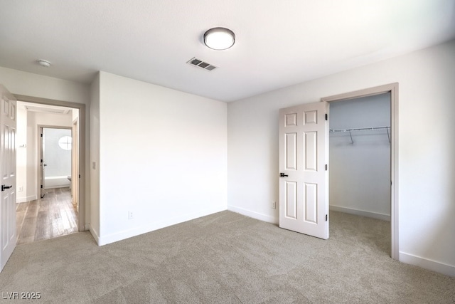 unfurnished bedroom with light colored carpet, a closet, and a spacious closet