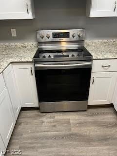 kitchen with white cabinetry, light wood-type flooring, light stone counters, and electric stove