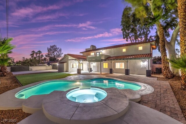 pool at dusk featuring a yard, an in ground hot tub, and a patio area