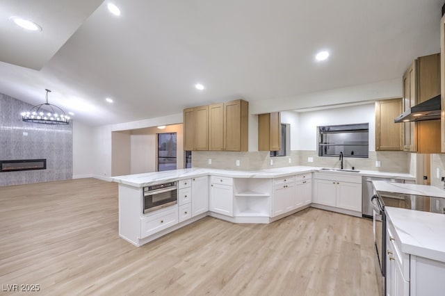 kitchen with sink, a fireplace, light hardwood / wood-style floors, kitchen peninsula, and decorative backsplash