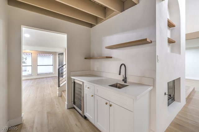 kitchen with sink, white cabinets, beverage cooler, and light hardwood / wood-style floors