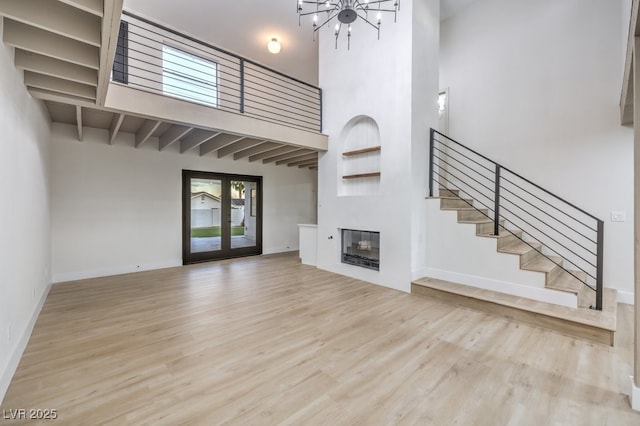 unfurnished living room with a towering ceiling, french doors, light hardwood / wood-style floors, and a chandelier