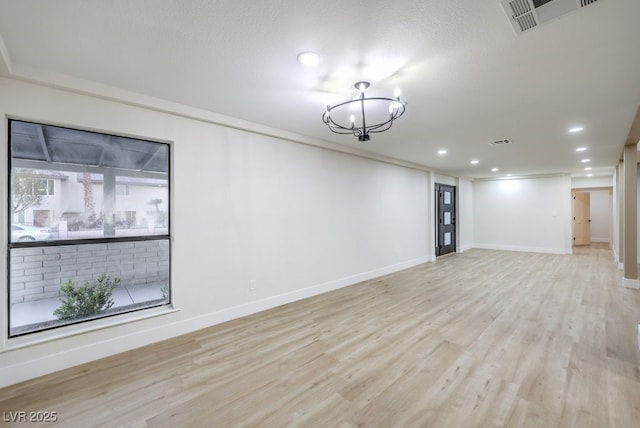 spare room featuring an inviting chandelier, light hardwood / wood-style floors, and crown molding