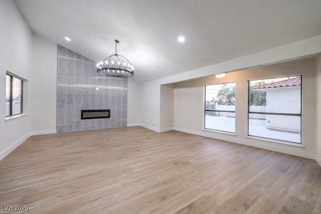 unfurnished living room featuring lofted ceiling, a tile fireplace, light hardwood / wood-style floors, and a notable chandelier