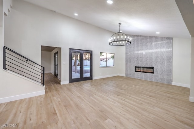 unfurnished living room featuring a tile fireplace, french doors, lofted ceiling, light wood-type flooring, and an inviting chandelier