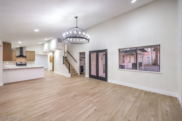 unfurnished living room featuring french doors, a high ceiling, an inviting chandelier, and light hardwood / wood-style floors