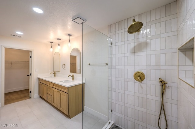 bathroom featuring a textured ceiling, a tile shower, and vanity