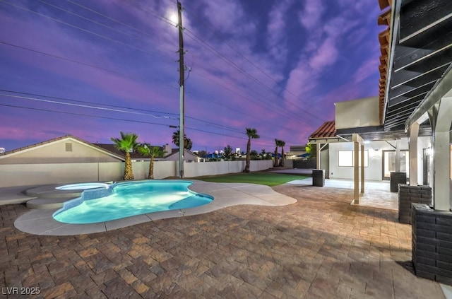 pool at dusk with a patio area and an in ground hot tub