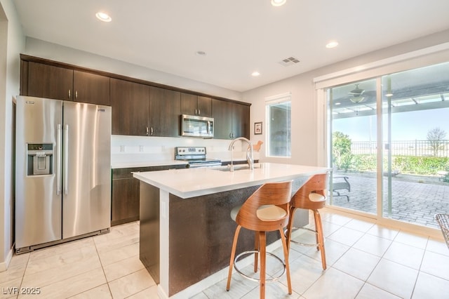 kitchen with stainless steel appliances, a center island with sink, and dark brown cabinetry