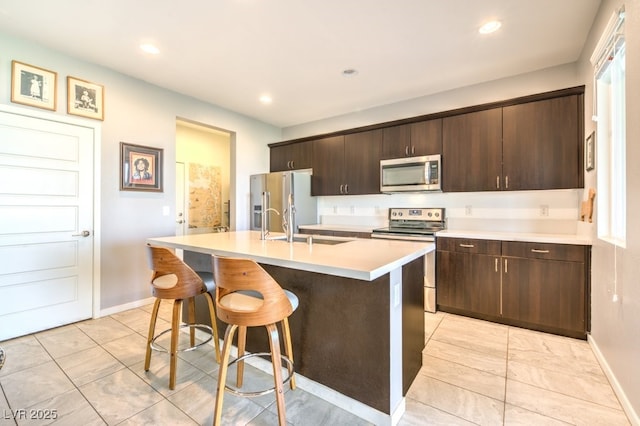 kitchen featuring a kitchen island with sink, appliances with stainless steel finishes, a breakfast bar, sink, and dark brown cabinets