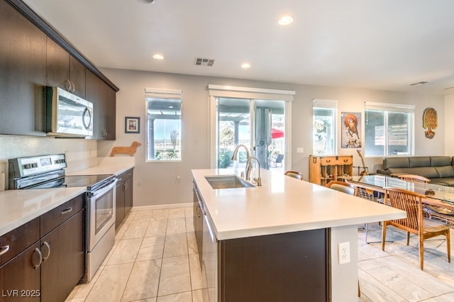 kitchen with stainless steel appliances, sink, dark brown cabinets, and an island with sink