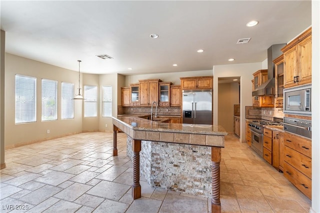 kitchen featuring built in appliances, a large island, wall chimney exhaust hood, tasteful backsplash, and a breakfast bar area