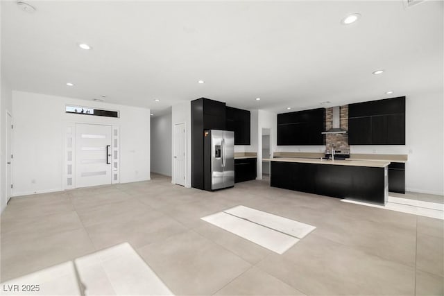 kitchen with a kitchen breakfast bar, an island with sink, stainless steel fridge, sink, and wall chimney range hood