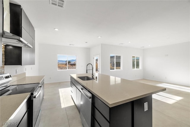 kitchen with appliances with stainless steel finishes, wall chimney range hood, sink, and an island with sink